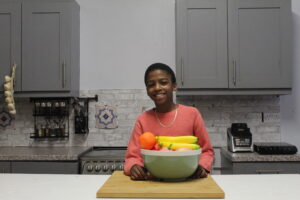 Vegan chef and CEO Omari McQueen in his kitchen with a bowl of fruit. 