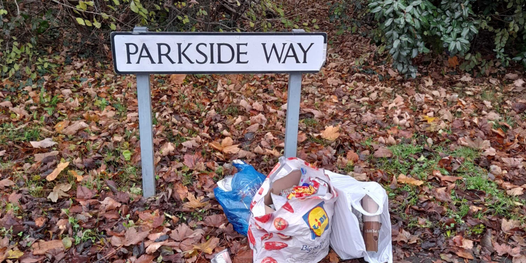 Image shows a sign for the street Parkside Way with several garbage-filled plastic bags piled up next to it.